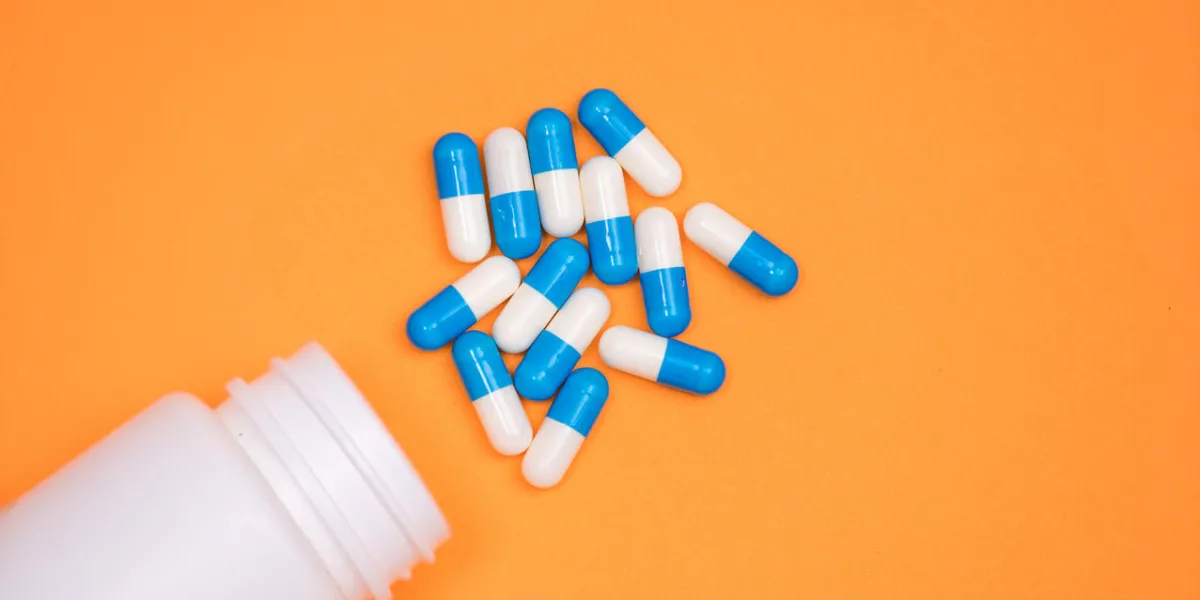 antibiotic medical drug capsule falling from bottle on orange background antibiotic medical drug capsule falling from bottle on orange background
