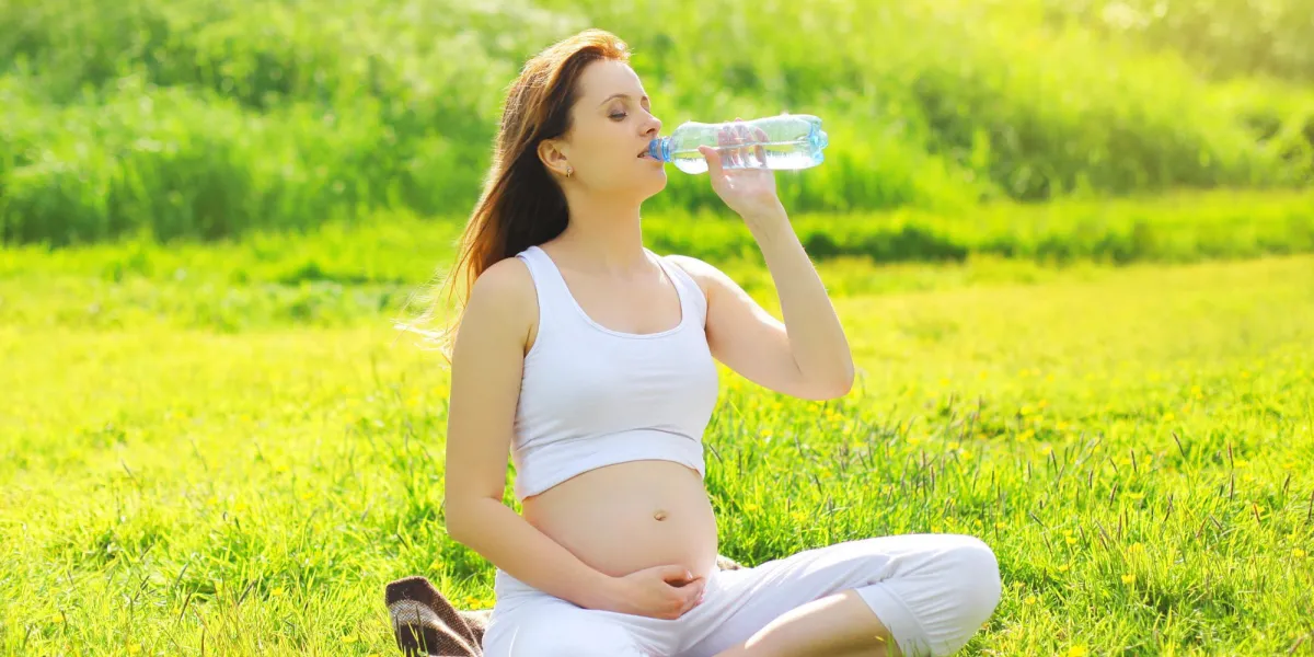 grossesse, sport et santé mode de vie - jeune femme enceinte l'eau potable d'une bouteille assis sur l'herbe dans la journée d'été ensoleillée grossesse, sport et santé mode de vie - jeune femme enceinte l'eau potable d'une bouteille assis sur l'herbe dans la journée d'été ensoleillée