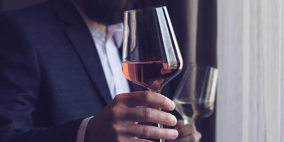 horizontal close up of a caucasian man with beard black suit and white shirt offering a tall glass of rose wine at an event by the window natural light horizontal close up of a caucasian man with beard black suit and white shirt offering a tall glass of rose wine at an event by the window natural light