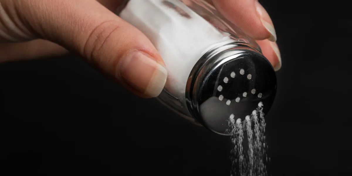 female hand pouring salt from salt shaker on black background