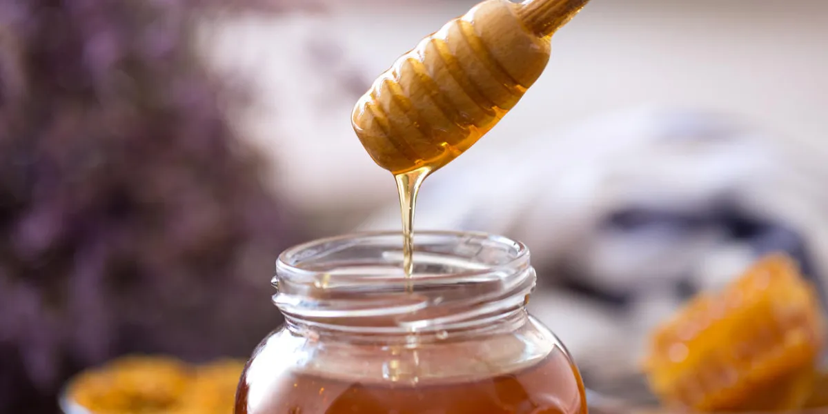 dripping sweet fresh honey from wooden dipper background