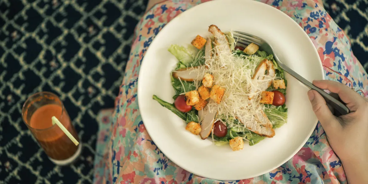 a plate with a salad on female knees and glass of carrot juice view from above the concept of food and healthy lifestyles