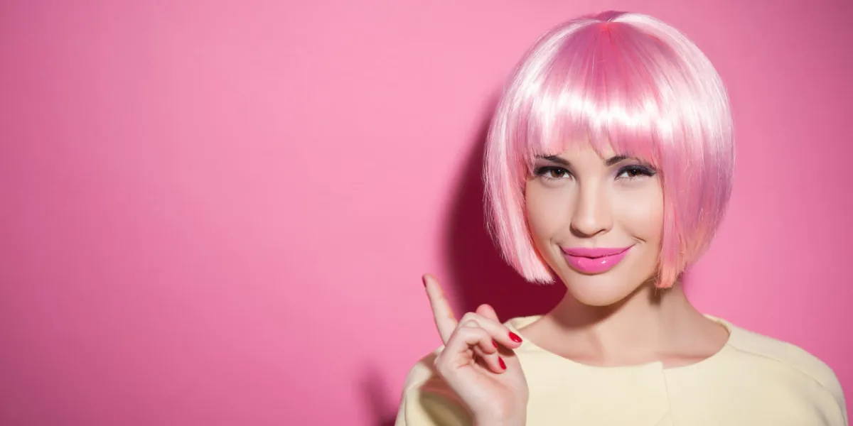 let me show you something interesting portrait of beautiful girl pointing finger up with confidence she is standing in pink wig and smiling isolated and copy space in left side