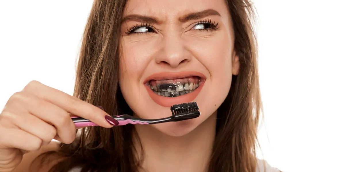 young woman brushing her teeth with a black tooth paste with active charcoal, and black tooth brush on white background