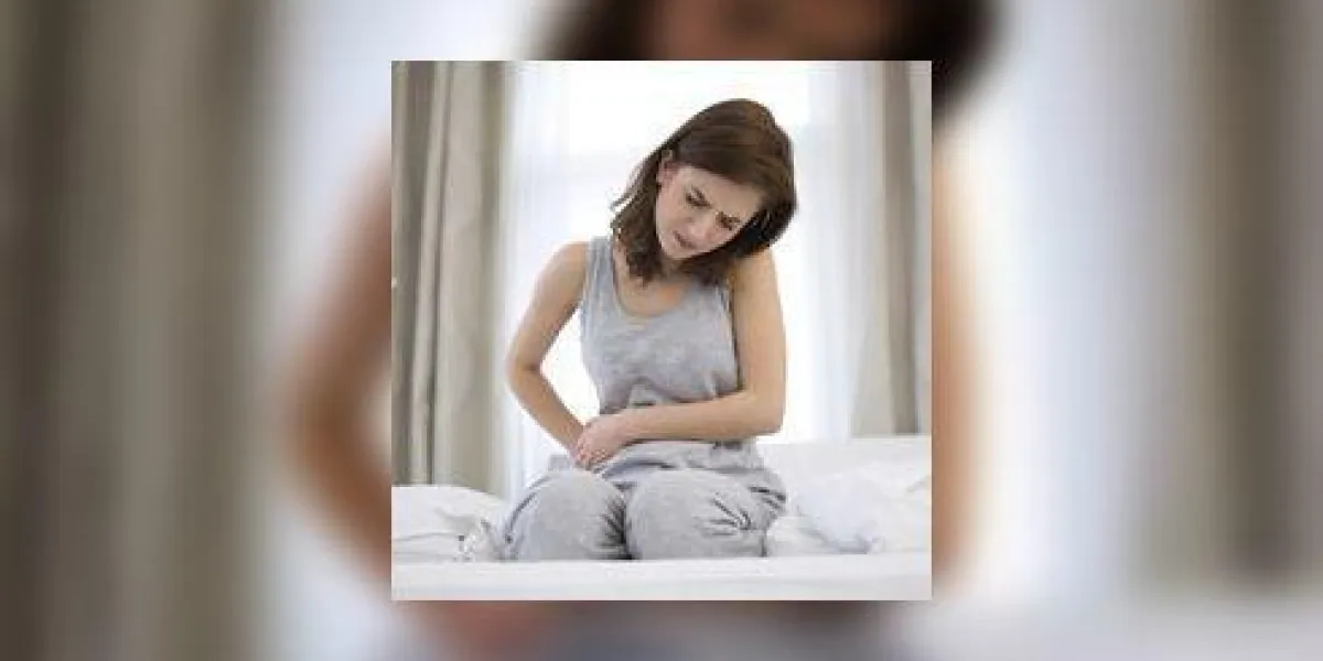 jeune femme assise sur le lit avec douleur dans l'estomac