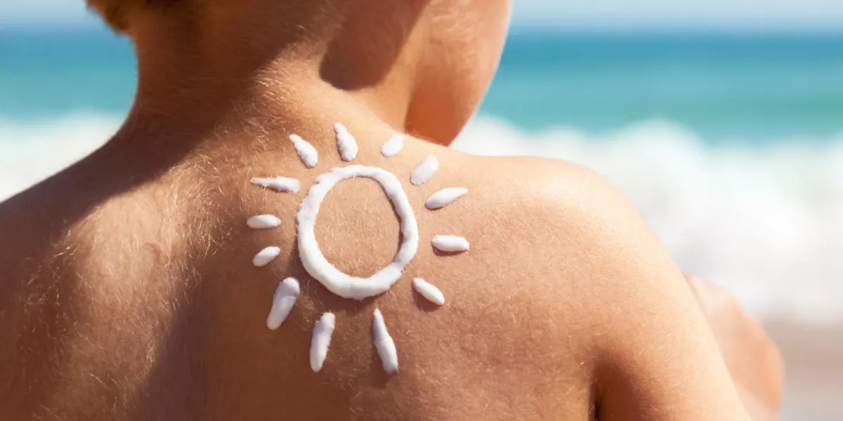 child with suntan lotion shaped as a sun on his back at the beach concept for sun protection and skin care for children