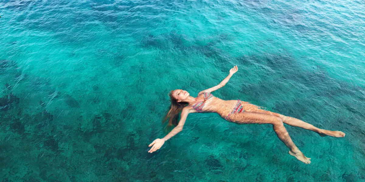young slim woman lie on back and relaxing in blue sea water