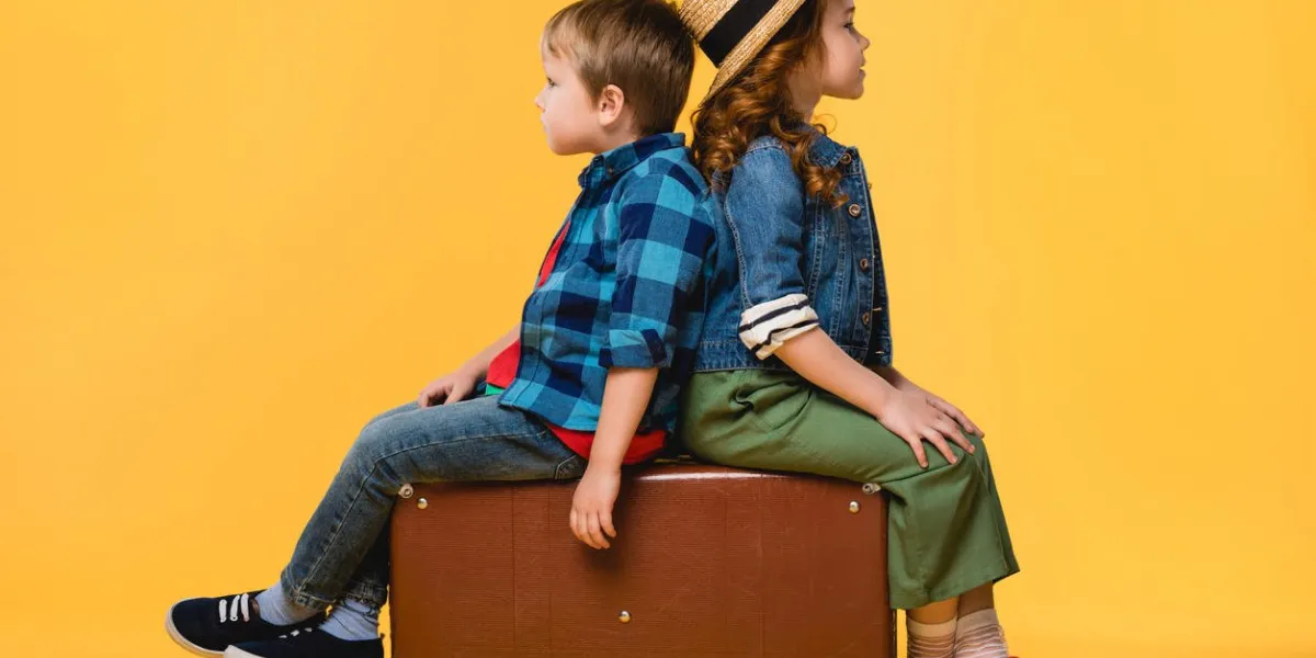 side view of children sitting on leather suitcase isolated on yellow