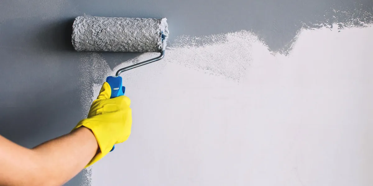 hand in yellow glove painting wall in gray color with a roller brush