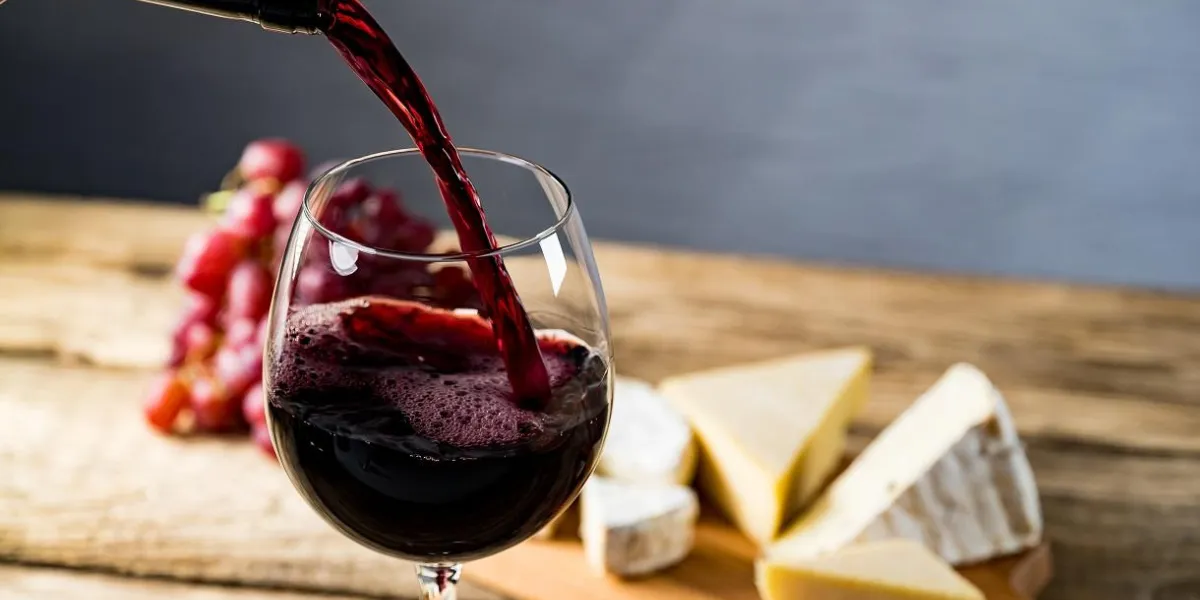 pouring red wine into the glass against wooden table pouring red wine into the glass against wooden table