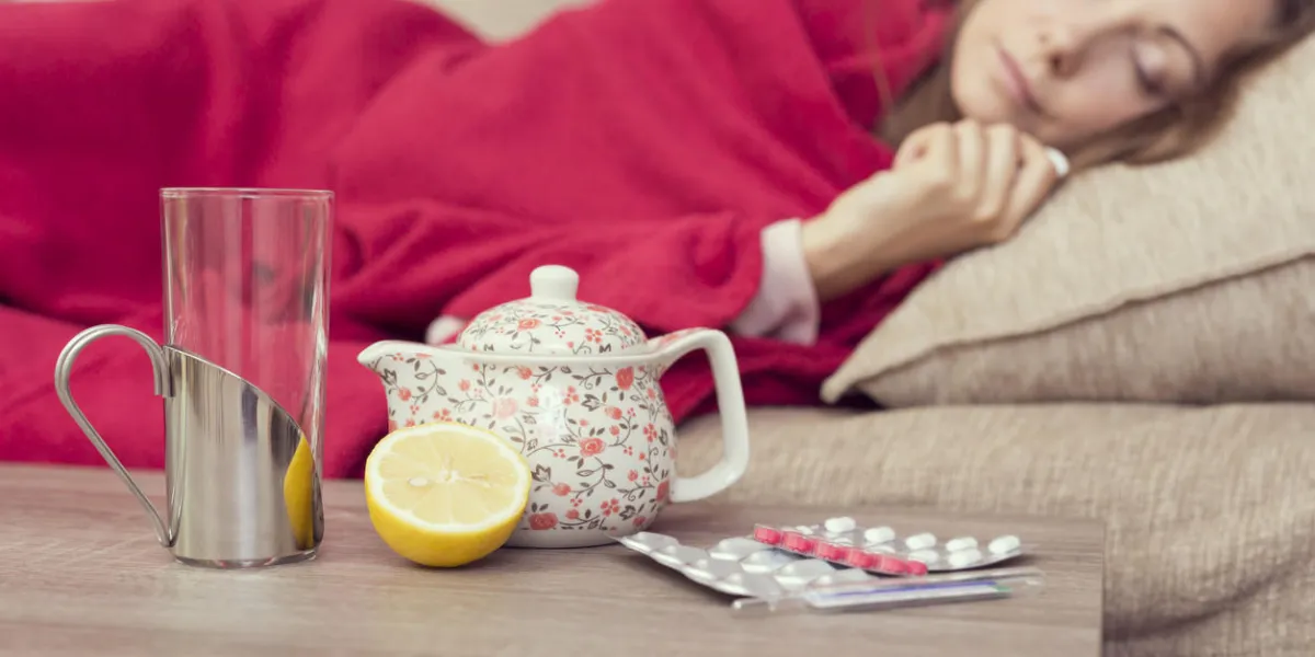 femme malade recouverte d'une couverture couchée dans son lit avec une forte fièvre et une grippe, théière au repos, des pilules et du citron sur la table, se concentrer sur le citron et une théière
