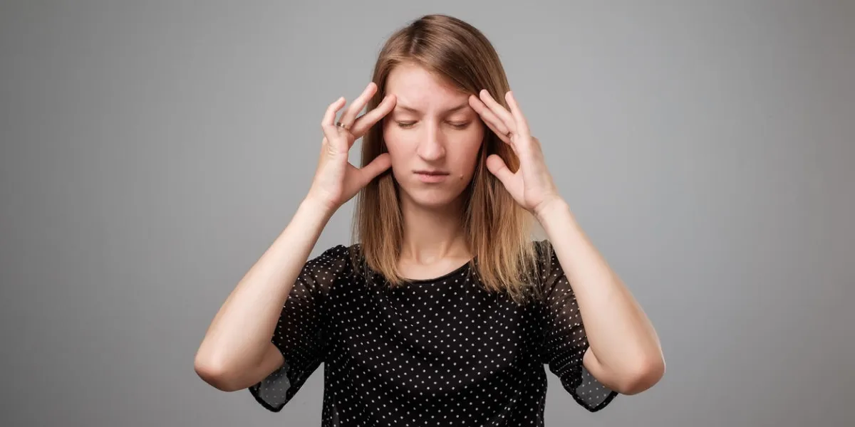 portrait of beautiful young woman touching her temples feeling stress, on gray background portrait of beautiful young woman touching her temples feeling stress, on gray background