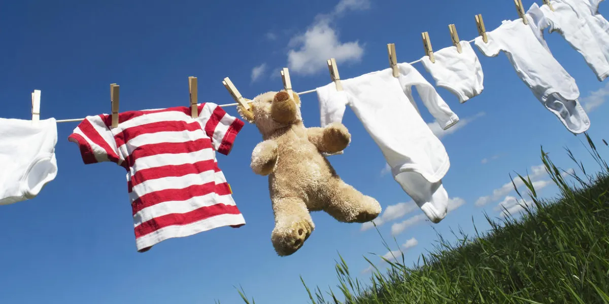 vêtements pour bébés et un ours en peluche sur une corde à linge vers le ciel bleu