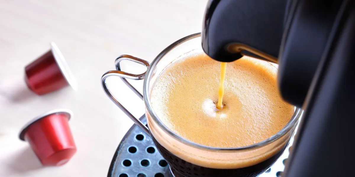 machine à servir du café expresso dans une tasse en verre et deux capsules sur la table