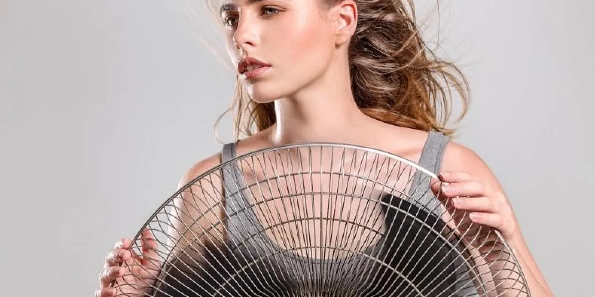 young woman cooling face under wind of cooler fan isolated on white background