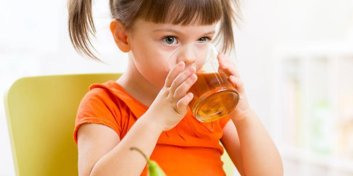 souriante enfant fille assise sur la table avec des fruits et de boire du jus en pépinière