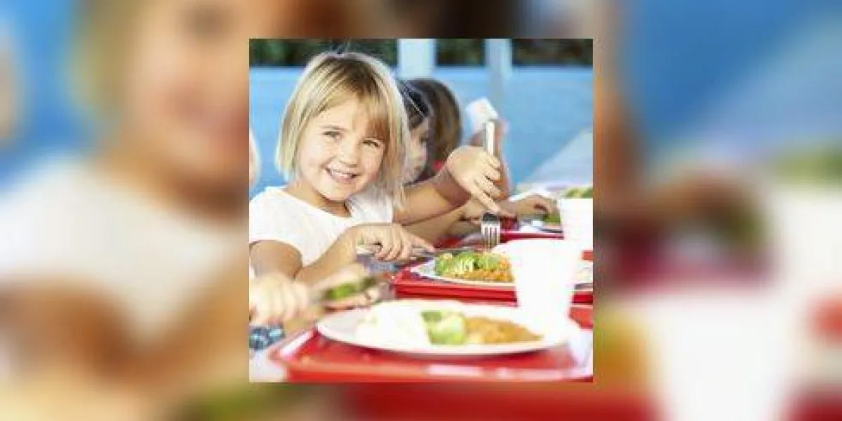 Élèves élémentaires bénéficiant d'un déjeuner sain à la cafétéria assis souriant à la caméra