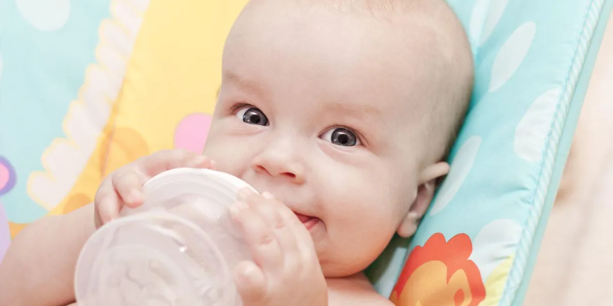 bébé heureux tenant une bouteille et boire de l'eau en regardant la caméra
