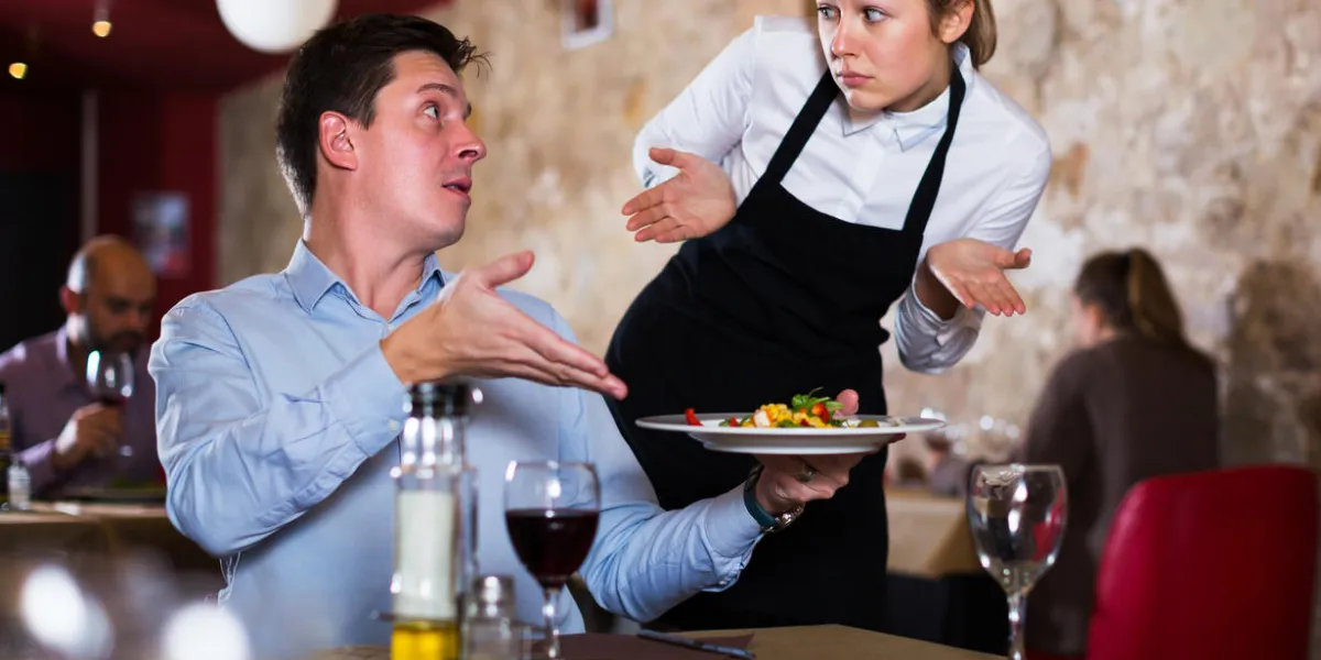 dissatisfied man expressing displeasure with food talking to excusing waitress in restaurant focus on man dissatisfied man expressing displeasure with food talking to excusing waitress in restaurant focus on man