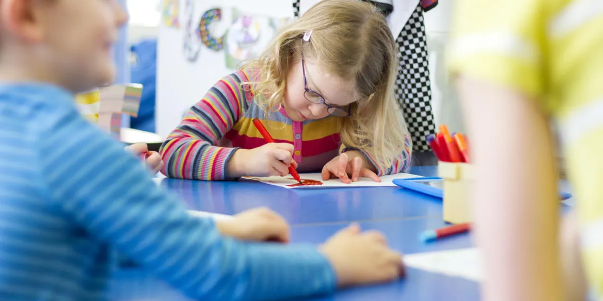 little girl sitting at a table in her nursery classroom she is colouring in with felt tip pens