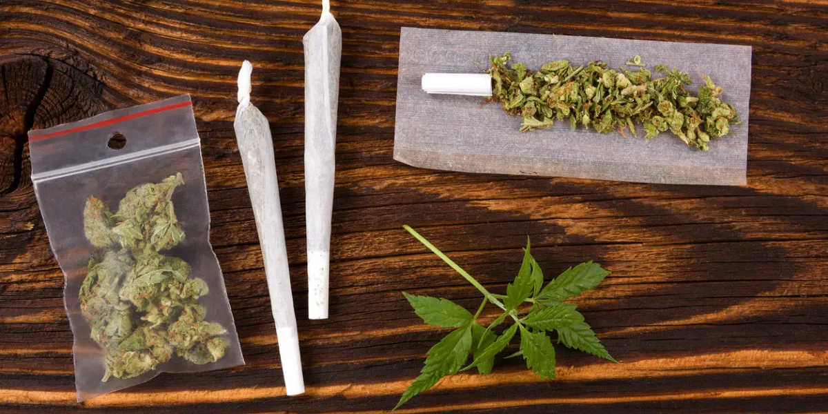 marijuana background cannabis joint, bud in plastic bag and hemp leaves on wooden table addictive drug or alternative medicine