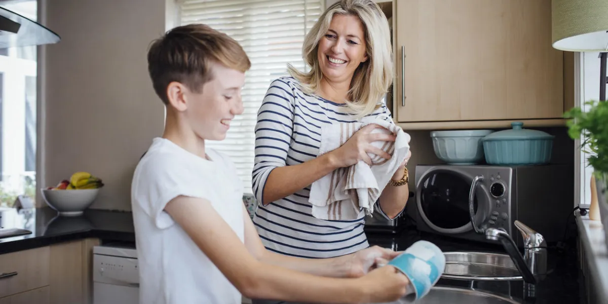 mother and son doing the dishes together they are talking and laughing as the boy washes and the mother dries dishes