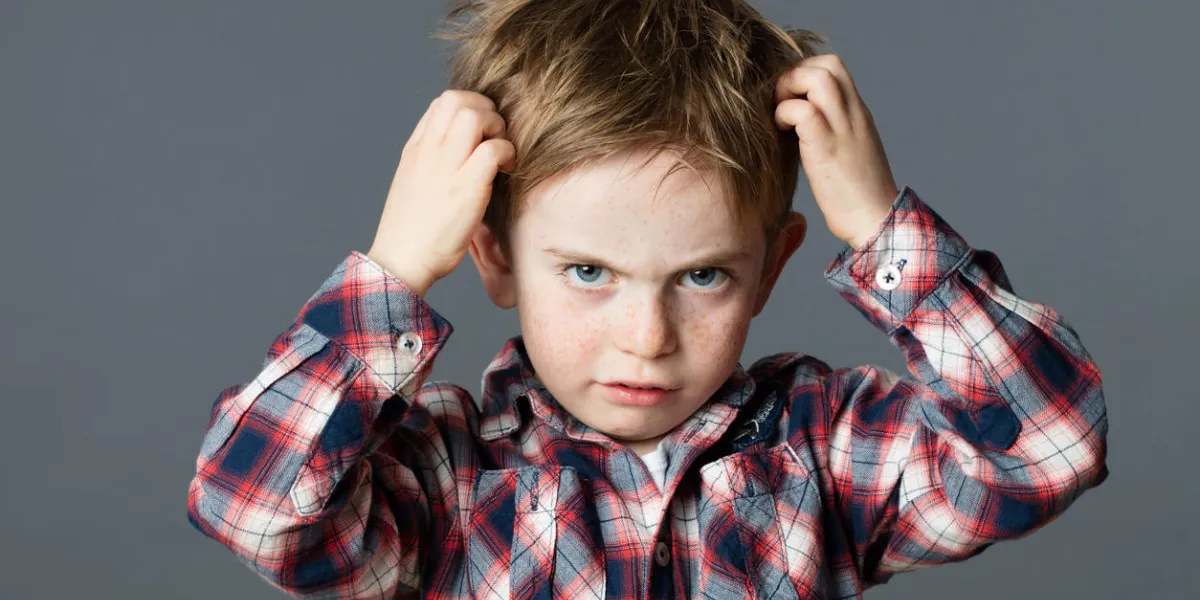 mischievous unhappy 6-year old kid with freckles scratching his hair for head lice or allergies, grey background studio