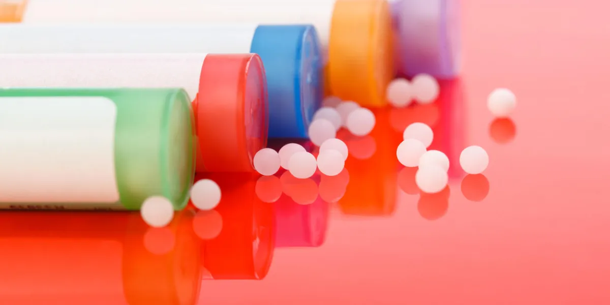 colorful homeopathic pills and containers on reflective red background