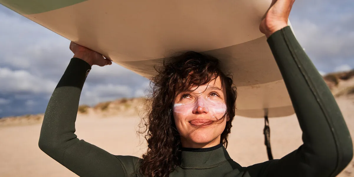 portrait of the cute woman with sunscreen at her chicks carrying surfboard on head and enjoying of the summer stock photo portrait of the cute woman with sunscreen at her chicks carrying surfboard on head and enjoying of the summer stock photo