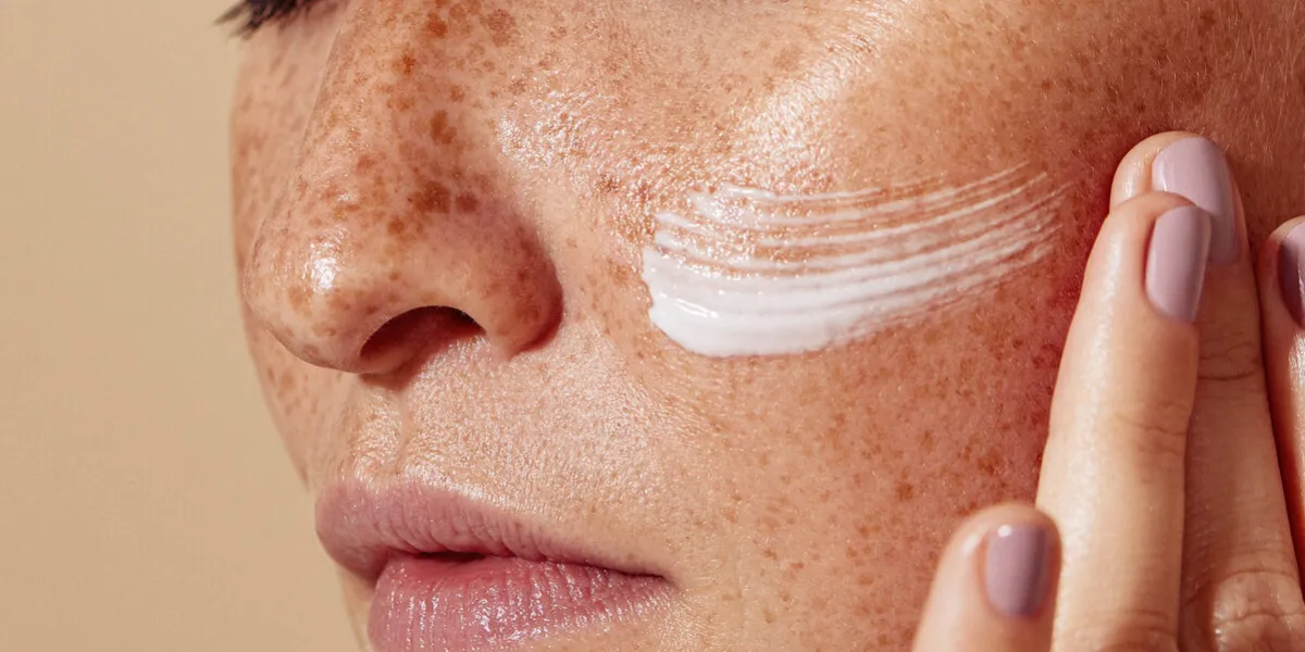 close-up of female face with freckled skin high-detailed shot of woman skin applying moisturizer