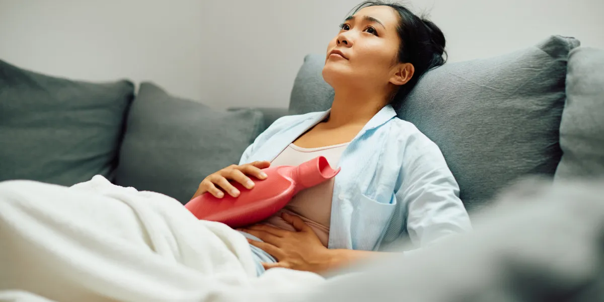 young asian woman holding hot water bottle on her stomach at home