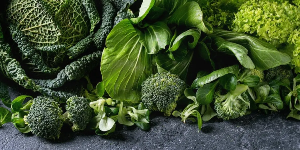 variety of raw green vegetables salads, lettuce, bok choy, corn, broccoli, savoy cabbage as frame over black stone texture background space for text