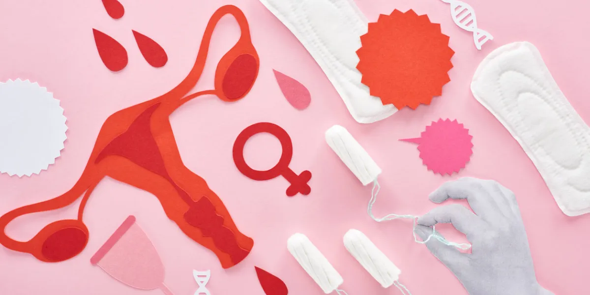 cropped view of white hand holding tampon on pink background with sanitary napkins, paper cut female reproductive internal organs and blood drops