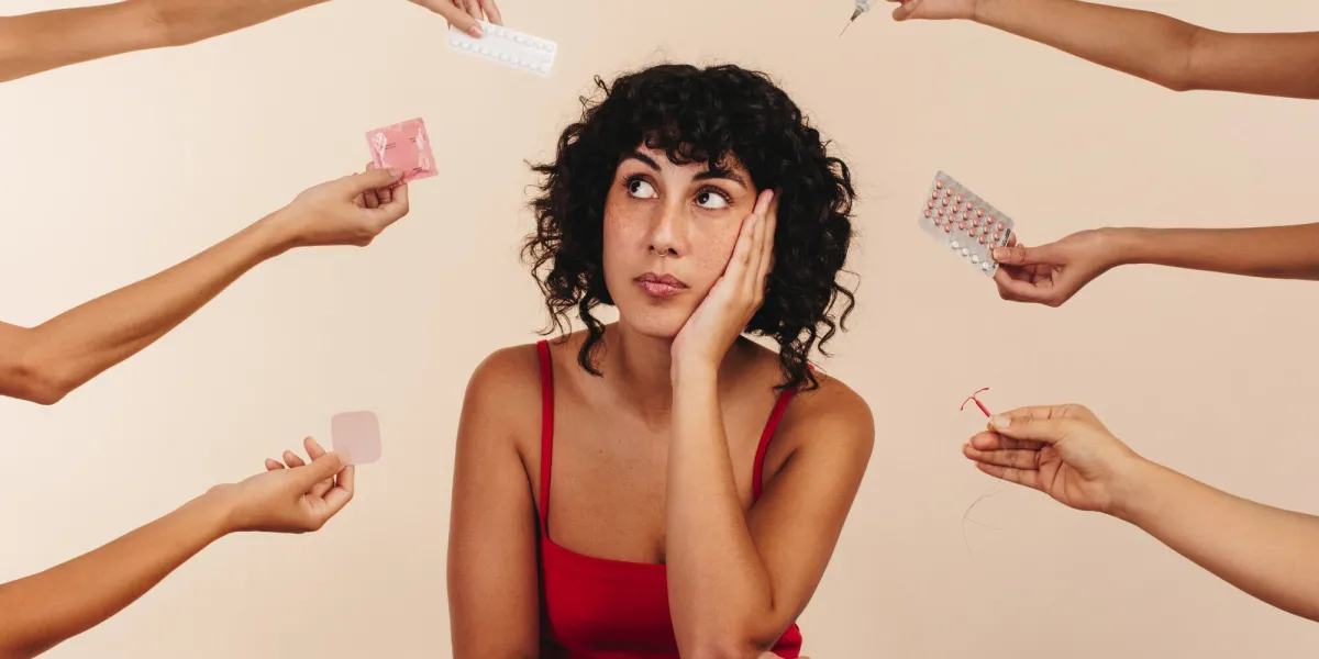 young woman looking away thoughtfully while surrounded by hands holding different forms of hormonal and non-hormonal contraception pensive young woman making a decision about her reproductive health