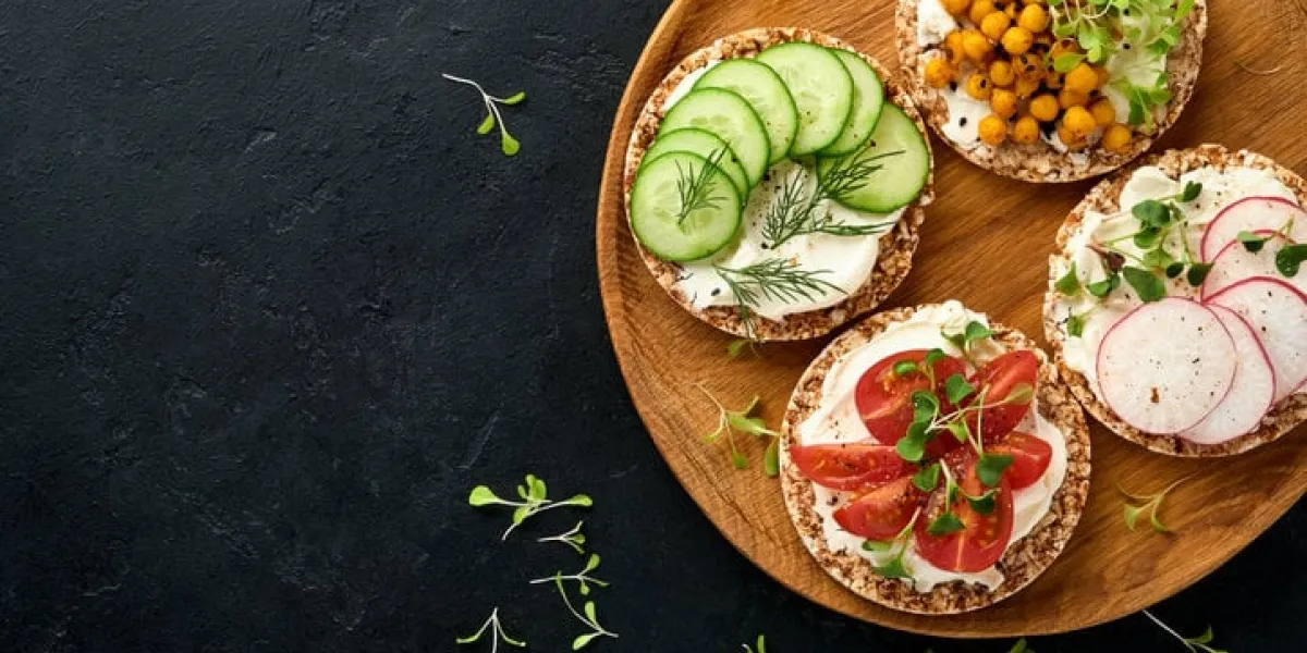 three crispy buckwheat bread gluten free with cream cheese, radish, tomato, cucumber, and microgreen for healthy breakfast on wooden stand on black stone background concept vegan and healthy eating