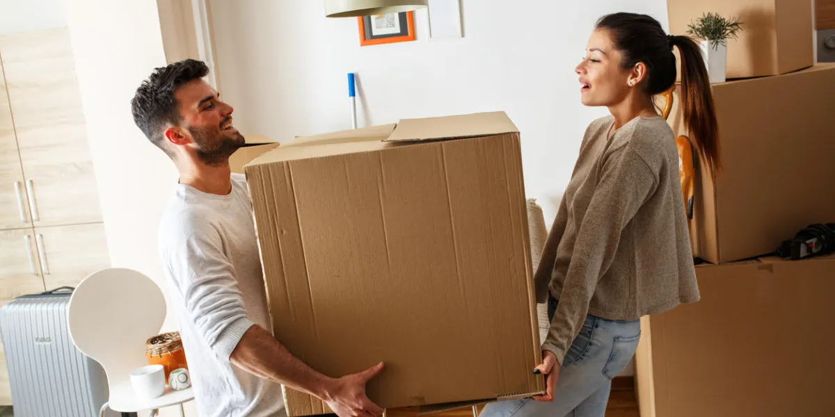 jeune couple transportant grande boîte en carton à la nouvelle maison homemoving