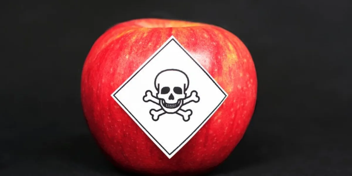 concept of pesticide residues in agricultural food products dangerous to humans, showing a red apple with poison symbol sticker on black background concept of pesticide residues in agricultural food products dangerous to humans, showing a red apple with poison symbol sticker on black background
