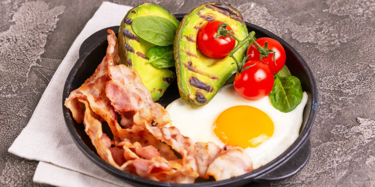 grilled bacon and avocado, fried eggs with spinach and cherry tomatoes on vintage wooden cutting board gray concrete background ketogenic diet low carb high fat breakfast healthy food concept