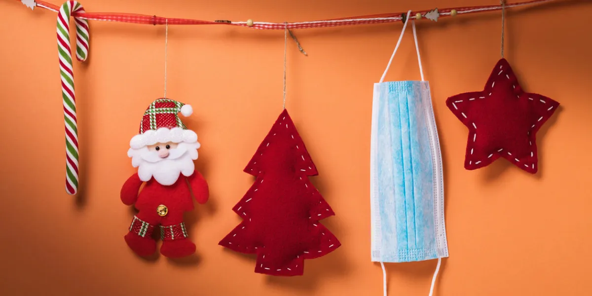 christmas decorations and a medical mask hang on a decorative ribbon on a colored background quarantine concept for the new year christmas decorations and a medical mask hang on a decorative ribbon on a colored background quarantine concept for the new year