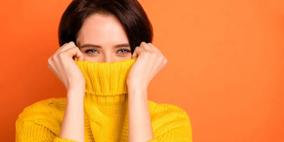 close up photo of cute nice, charming girl hiding from cold by wrapping up in collar while isolated with orange background