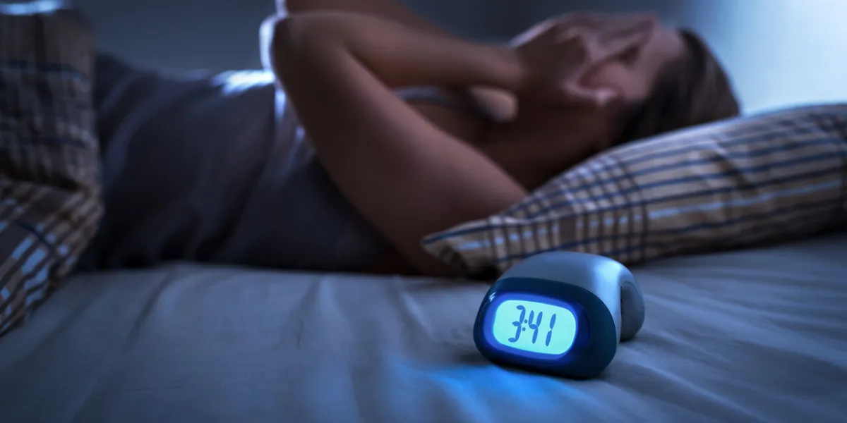 sleepless woman suffering from insomnia, sleep apnea or stress tired and exhausted lady headache or migraine awake in the middle of the night frustrated person with problem alarm clock with time