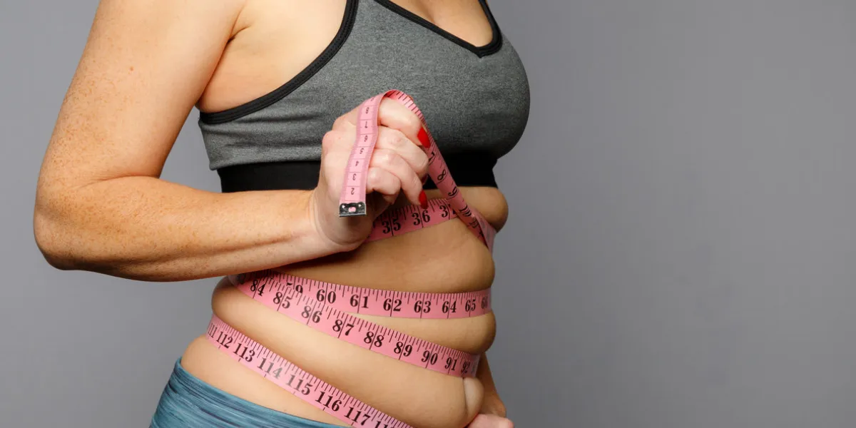 woman in active wear with squeezed measuring tape on a gray background woman in active wear with squeezed measuring tape on a gray background