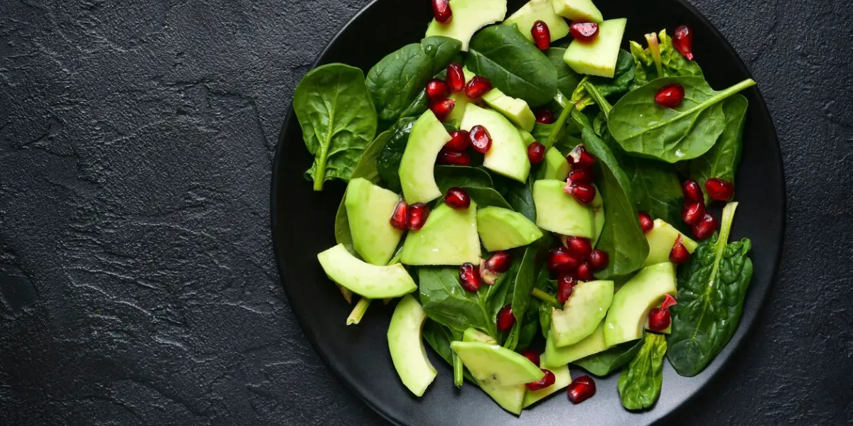 avocado salad with baby spinach and pomegranate on a black plate on a slate,stone or concrete backgroundtop view with copy space avocado salad with baby spinach and pomegranate on a black plate on a slate,stone or concrete backgroundtop view with copy space