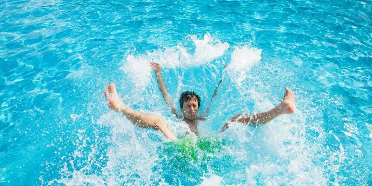 homme tombant et éclaboussant dans l'eau de la piscine
