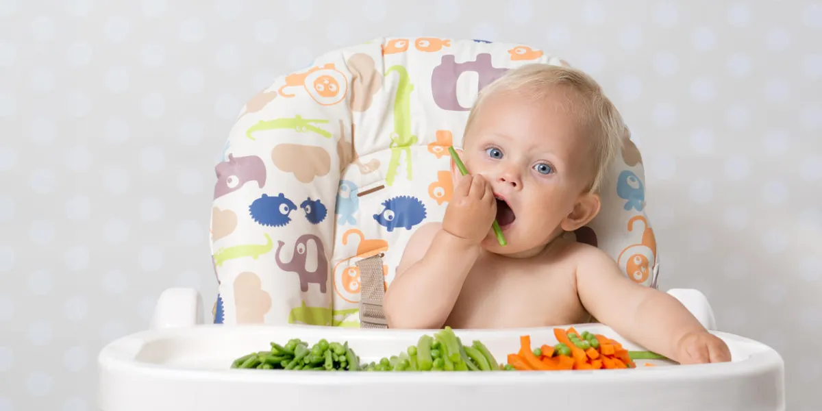bébé fille assise dans une chaise haute, mangeant des légumes crus et de saison carottes, haricots, pois, céleri bébé fille assise dans une chaise haute, mangeant des légumes crus et de saison carottes, haricots, pois, céleri