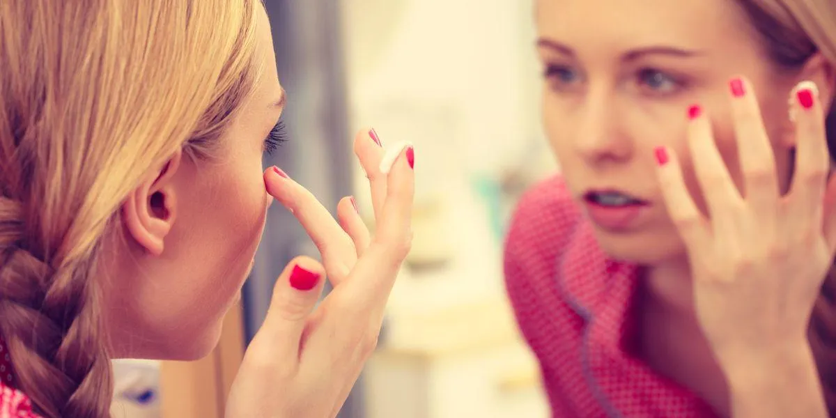 young blonde woman applying moisturizing skin cream on face, looking in bathroom mirror girl taking care of dry complexion layering moisturizer skincare treatment young blonde woman applying moisturizing skin cream on face, looking in bathroom mirror girl taking care of dry complexion layering moisturizer skincare treatment
