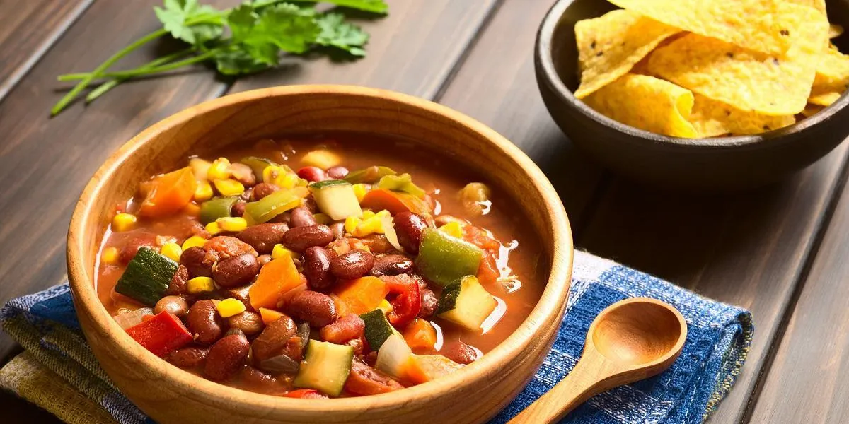 bol en bois de chili végétarien fait avec haricot, carotte, courgette, poivron, maïs sucré, tomate, oignon, ail, avec des chips tortilla dans le dos, photographié avec la lumière naturelle (mise au point sélective, mise au point au milieu du plat) bol en bois de chili végétarien fait avec haricot, carotte, courgette, poivron, maïs sucré, tomate, oignon, ail, avec des chips tortilla dans le dos, photographié avec la lumière naturelle (mise au point sélective, mise au point au milieu du plat)