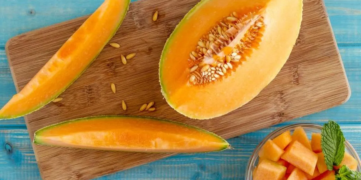 organic cut cantaloupe melon slices siting on wooden cutting board with seeds and bowl of cut melon