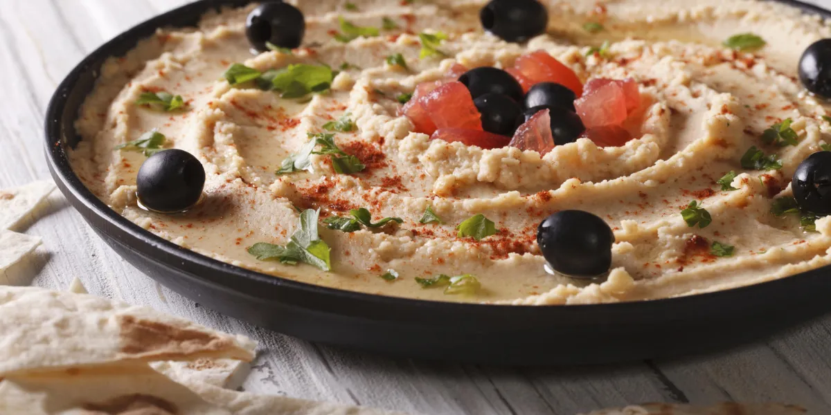 houmous maison aux olives et aux herbes sur une plaque close-up horizontal