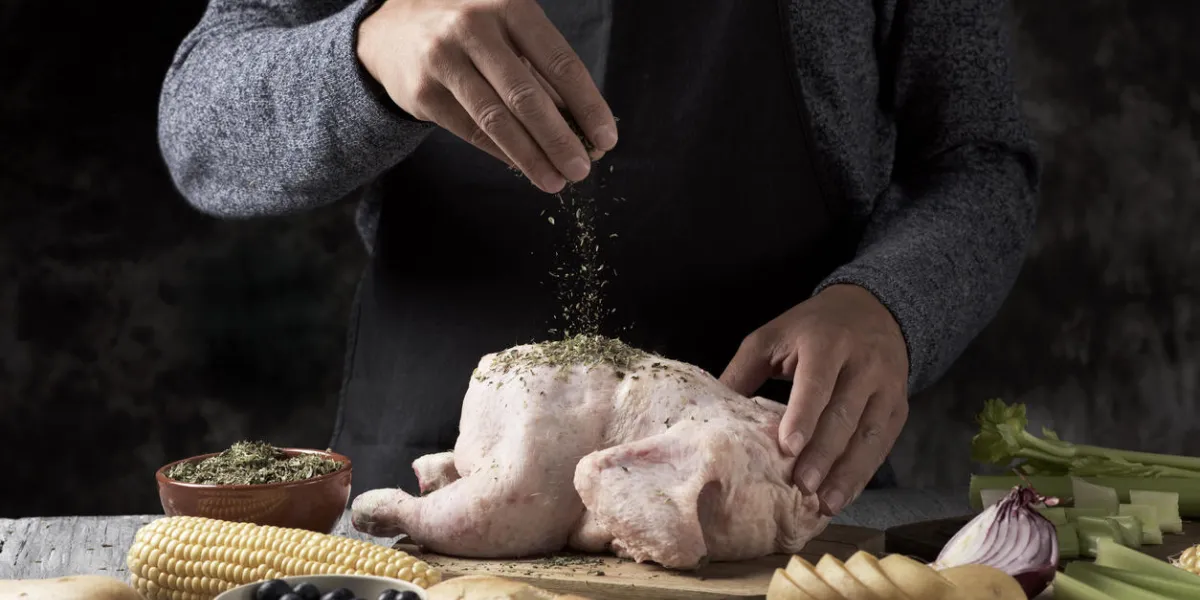 gros plan d'un jeune homme caucasien préparant une dinde placée sur une table en bois rustique pleine d'ingrédients pour le farcir comme la pomme, l'oignon ou différentes épices, et le céleri ou un maïs rôti en épi gros plan d'un jeune homme caucasien préparant une dinde placée sur une table en bois rustique pleine d'ingrédients pour le farcir comme la pomme, l'oignon ou différentes épices, et le céleri ou un maïs rôti en épi